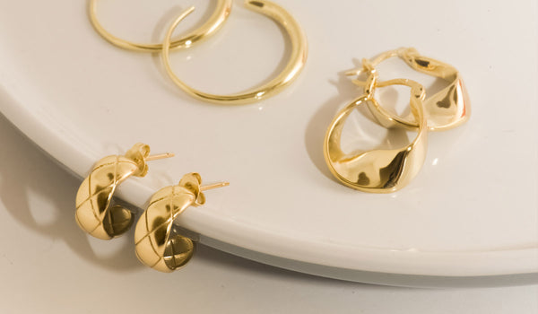 A stunning display of three pairs of trendy and stylish gold earrings elegantly arranged on a sleek plate.