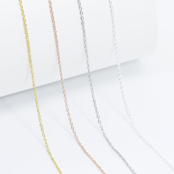 close up shot of four thin, minimalistic cable chain style layering necklaces in silver, frosted silver, gold and rose gold 
