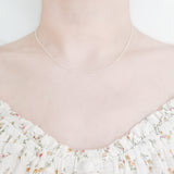 close up of female neck and collarbone area wearing a pretty floral top and a thin, minimalistic cable chain style layering necklaces in frosted silver