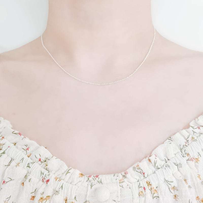 close up of female neck and collarbone area wearing a pretty floral top and a thin, minimalistic cable chain style layering necklaces in frosted silver