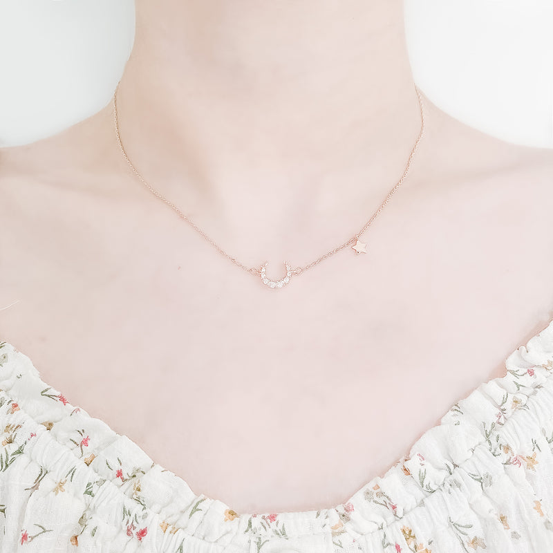 close up shot of neck and collarbone area of female wearing pretty floral top and a dainty gold plated necklace featuring a large moon shaped pendant made up from cubic zircona stones and a smaller star pendant