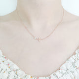 close up of a girl's neck and collarbone area wearing a pretty floral top and a delicate gold plated sterling silver necklaces featuring a small crossed star pendant and a cubic zirona stone