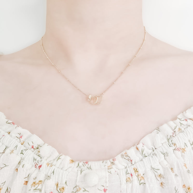 close up of a girl's neck and collarbone area wearing a pretty floral top and a delicate gold plated chain spaced with small beads and three small round charms