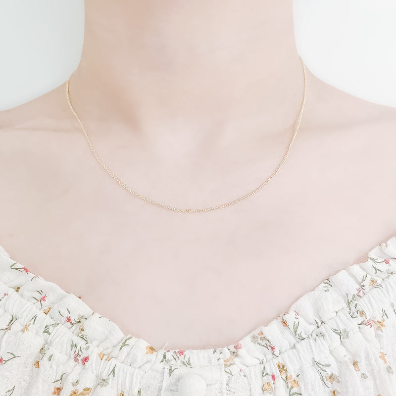 close up of female neck and collarbone area wearing a pretty floral top and a thin, minimalistic cable chain style layering necklaces in gold
