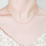 close up of female neck and collarbone area wearing a pretty floral top and a thin, minimalistic cable chain style layering necklaces in rose gold