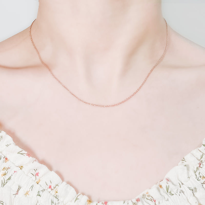 close up of female neck and collarbone area wearing a pretty floral top and a thin, minimalistic cable chain style layering necklaces in rose gold