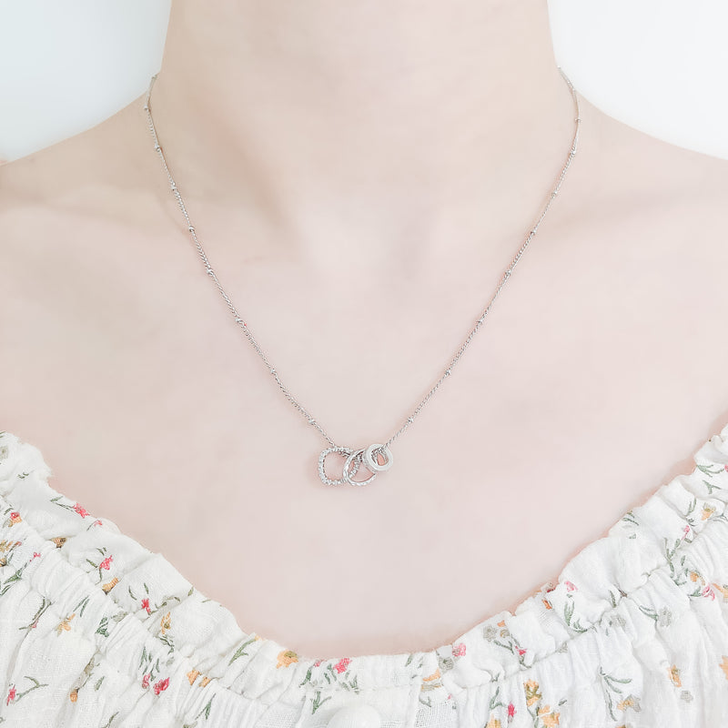 close up of a girl's neck and collarbone area wearing a pretty floral top and a delicate sterling silver chain spaced with small beads and three small round charms