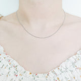 close up of female neck and collarbone area wearing a pretty floral top and a thin, minimalistic cable chain style layering necklaces in silver
