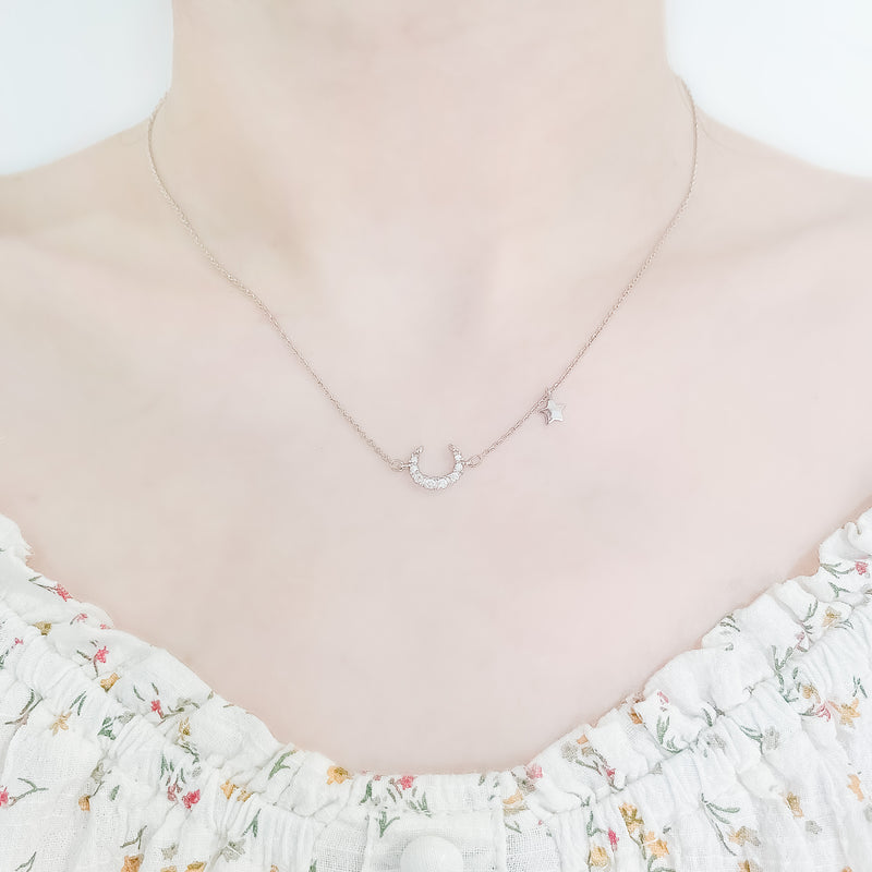 close up shot of neck and collarbone area of female wearing pretty floral top and a dainty sterling silver necklace featuring a large moon shaped pendant made up from cubic zircona stones and a smaller star pendant