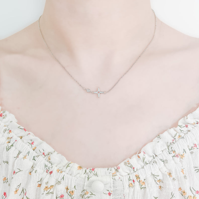 close up of a girl's neck and collarbone area wearing a pretty floral top and a delicate sterling silver necklaces featuring a small crossed star pendant and a cubic zirona stone