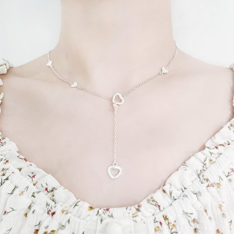 neck and collarbone shot of female wearing pretty floral top and romantic sterling silver chain necklace featuring two larger heart pendants and various small hearts throughout chain