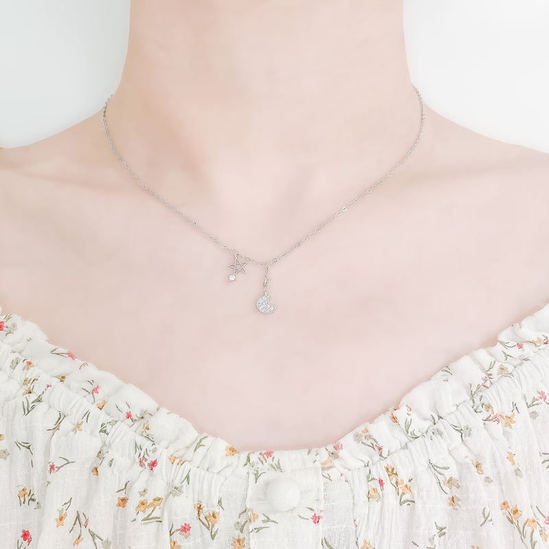 close up of girl's neck and collarbone wearing a pretty floral top and a cute sterling silver necklace featuring a small moon pendant made up of cubic zircona and a small star charm with a small cubic zircona stone attached